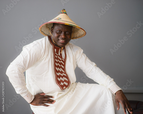 Handsome african man in traditional white dress and fulani hat on gray background photo