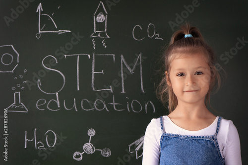 Schoolgirl stands near the blackboard on which is written "STEM education". She is holding a metal robot in her hands. The concept of modern learning. STEAM. DIY. AI.