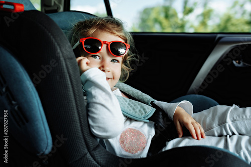 little cute girl in cap sitting in the car in child safety seat photo