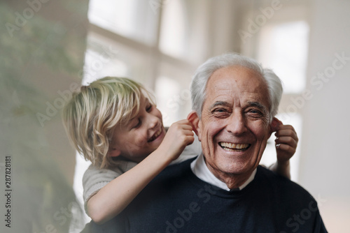 Happy grandson pulling grandfather's ears at home photo