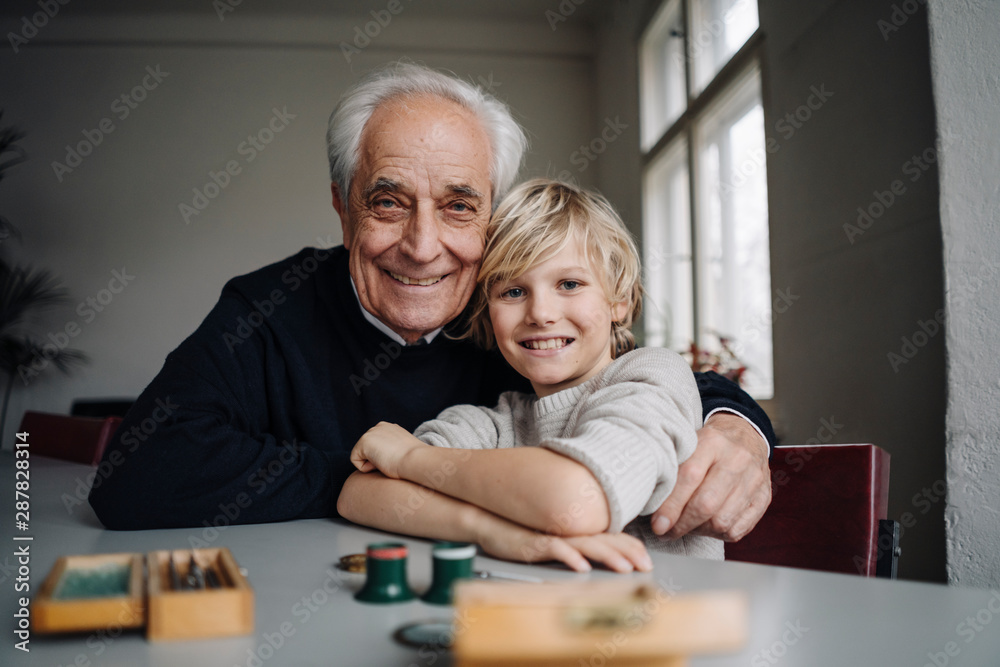 Portrait of happy watchmaker and his grandson sitting at table Portrait of happy watchmaker and his grandson sitting at table