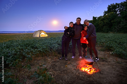 Family traveling and camping, twilight, cooking on the fire. Beautiful nature - field, forest, stars and moon.