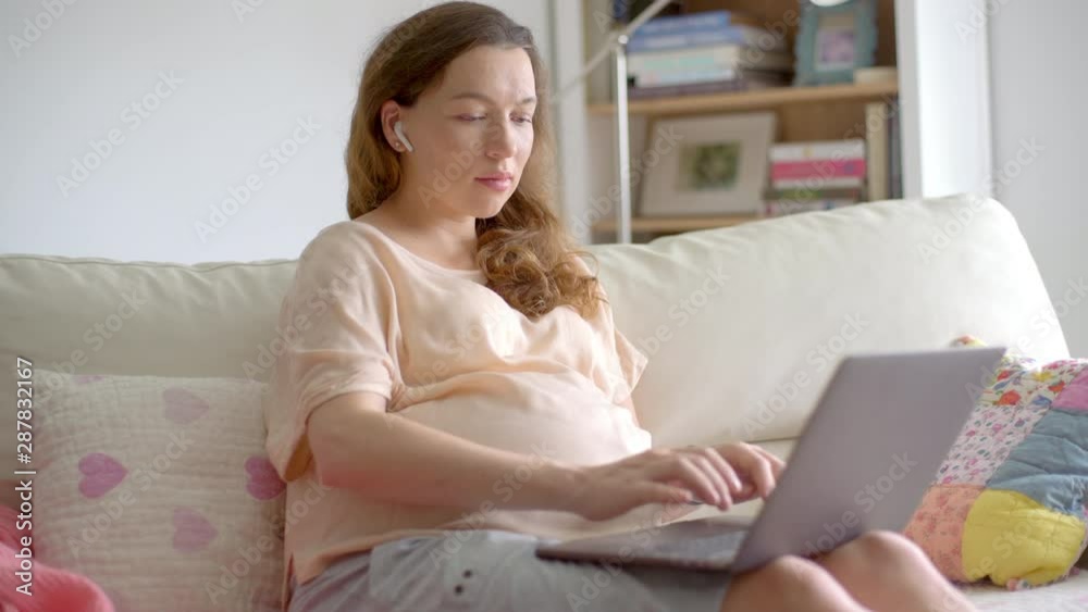Portrait of a young beautiful pregnant woman sitting on a sofa with a laptop computer in her hands. Pregnant businesswoman working online at home. Portrait of a young beautiful pregnant woman sitting on a sofa with a laptop computer in her hands. Pregnant businesswoman working online at home.