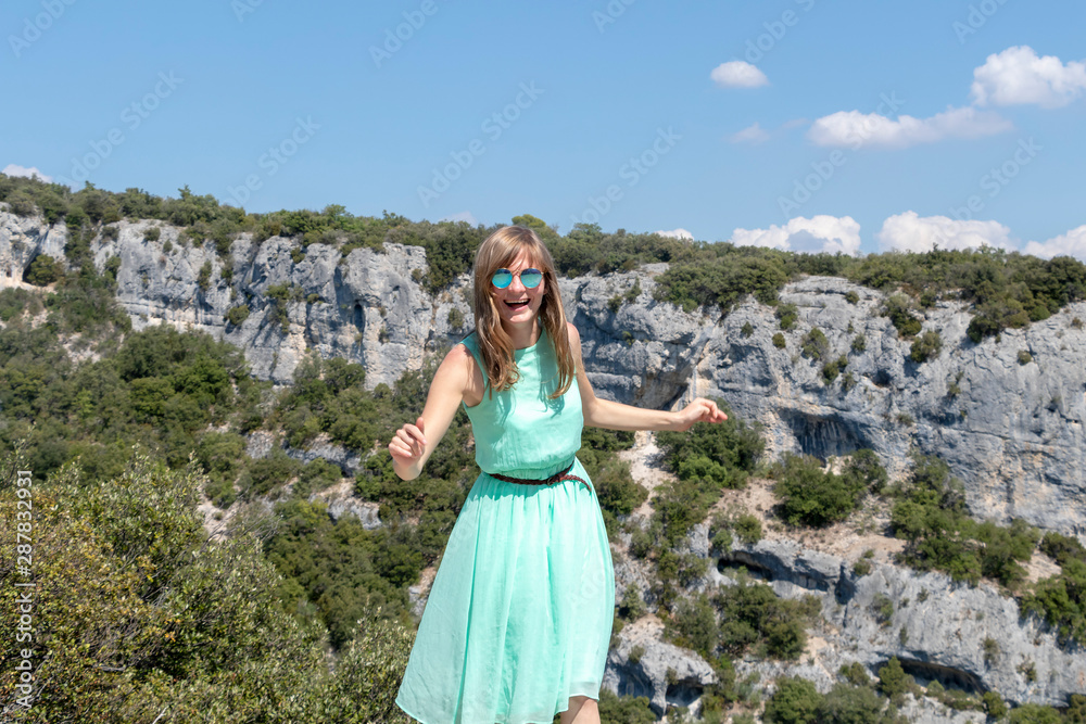 Naklejka premium Blond emotional female traveler at Canyon Gorges de la Nesque, gray cliffs with green forest in summer sunny day