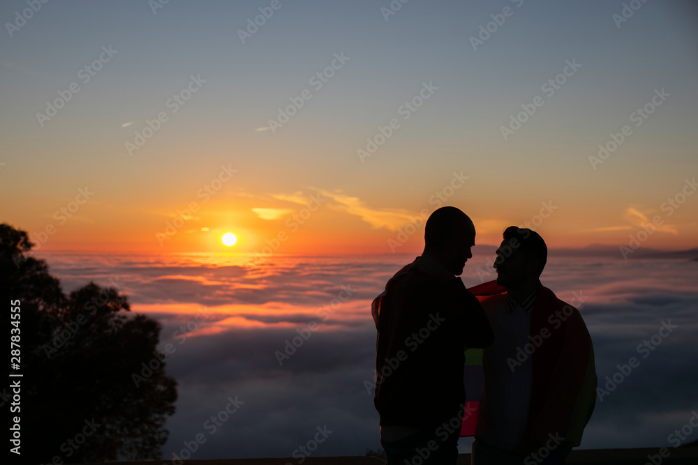 © Westend61 - Silhouette of gay couple with gay pride flag in backlight