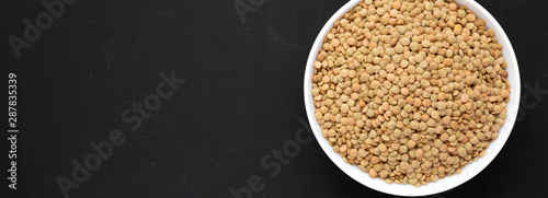 Organic green lentils in a white bowl on a black surface, overhead view. Flat lay, top view, from above. Copy space.