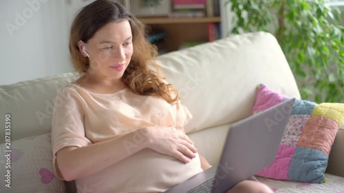 Portrait of a young beautiful pregnant woman sitting on a sofa with a laptop computer in her hands. Pregnant businesswoman working online at home.