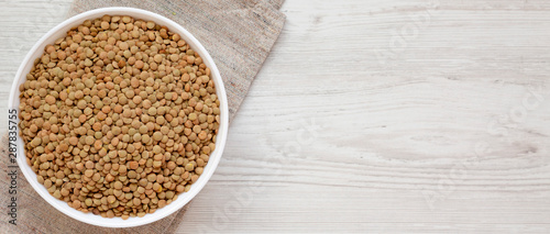 Organic green lentils in a white bowl on a white wooden surface  top view. Flat lay  overhead  from above. Copy space.