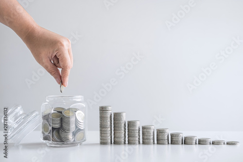 Hand putting coin into glass bottle money box for planning step and saving photo