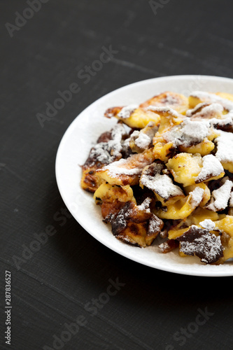 Homemade german Kaiserschmarrn pancake on a white plate on a black surface, side view. Copy space.