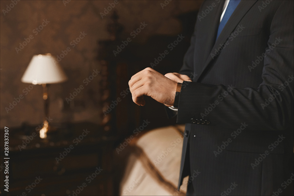 Close view of male hands with luxury watches of handsome young businessman in a stylish suit in the living room. Concept of official style and preparing for the business meeting