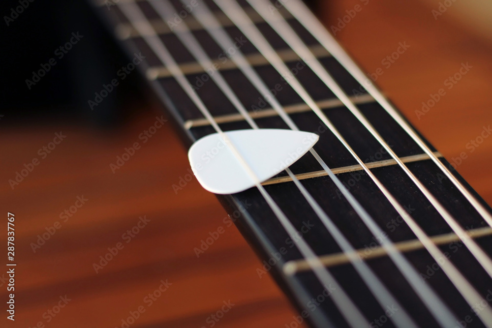 Fototapeta premium Guitar pick on the fingerboard of a brown guitar.