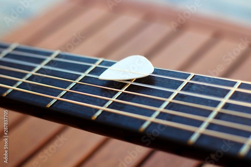 Guitar pick on the fingerboard of a brown guitar. photo