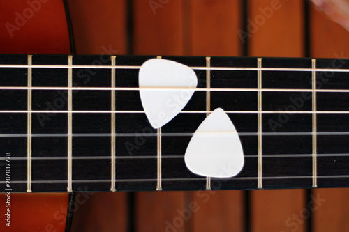 Guitar picks on the fingerboard of a brown guitar.