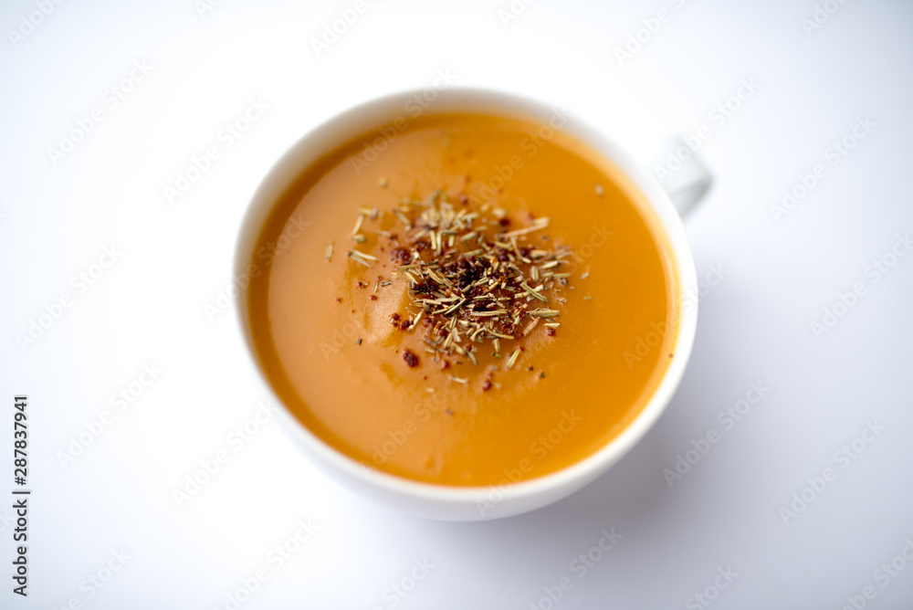Creamy pumpkin squash vegetable soup in a white cup on white background Creamy pumpkin squash vegetable soup in a white cup on white background