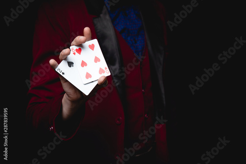 Magician shows focus, holds two playing cards in hand, copy space black background