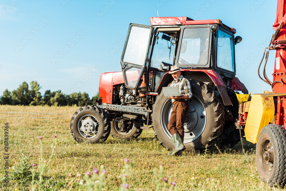 selective focus of bearded farmer in straw hat using laptop near tractor selective focus of bearded farmer in straw hat using laptop near tractor