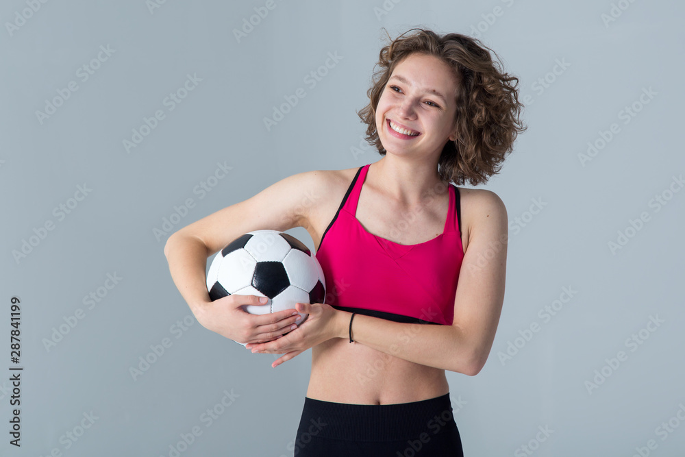 Young sports woman with a soccer ball in her hands standing on a gray background. Play female football. Young sports woman with a soccer ball in her hands standing on a gray background. Play female football.