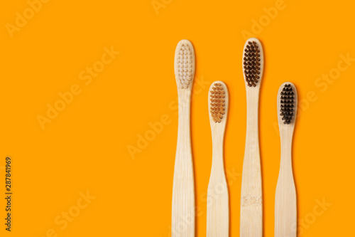 Four eco-friendly bamboo toothbrushes on a juicy orange background.. Copy space. Zero waste concept, plastic-free, organic, eco-friendly shopping