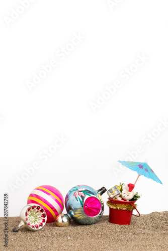 A group of Christmas decorations and a cocktail umbrella on sand with a white background.