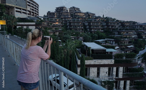 Young tourist, on the observation deck photographs a brown island hotel, in Budva, Montenegro