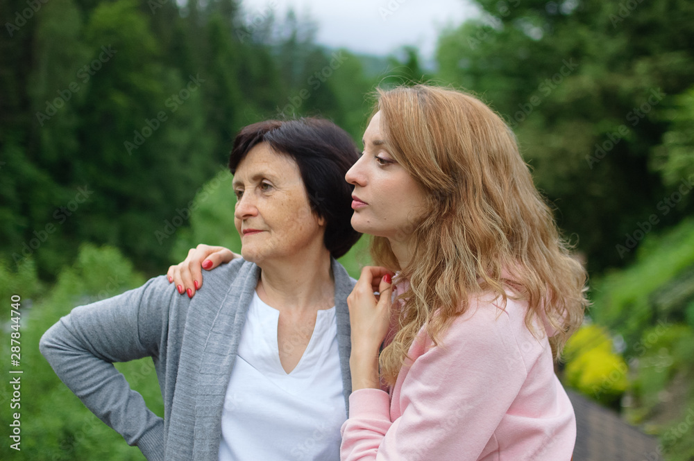 Outdoors portrait of happy senior woman and girl who are traveling together over landscape of forest and mountains. Concept of tenderness, care, family love, relationships. Outdoors portrait of happy senior woman and girl who are traveling together over landscape of forest and mountains. Concept of tenderness, care, family love, relationships.