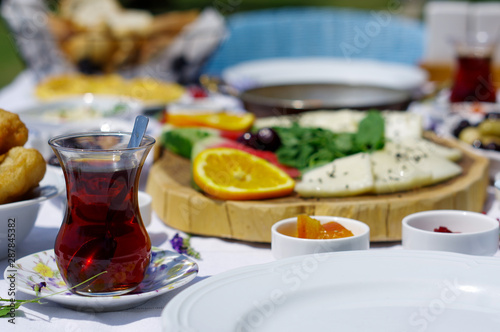 a glass of Turkish tea on a breakfast table next to some pastry and flowers