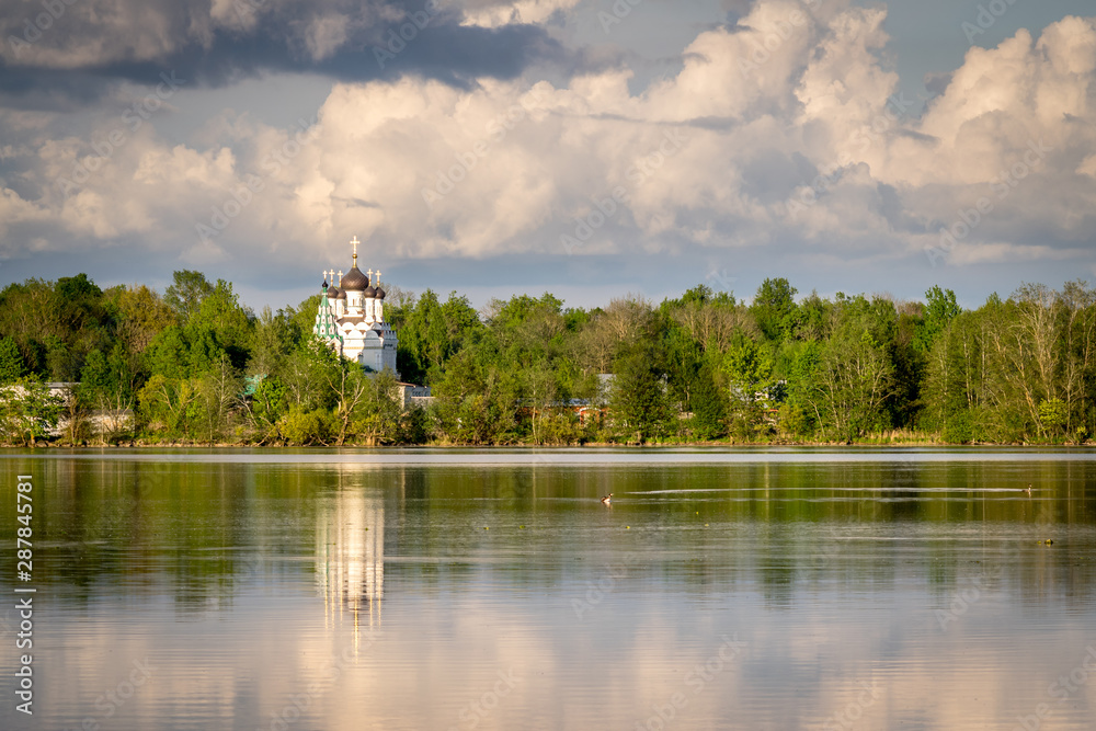 an Orthodox church amongst trees on a riverbank with reflections in the water. an Orthodox church amongst trees on a riverbank with reflections in the water.