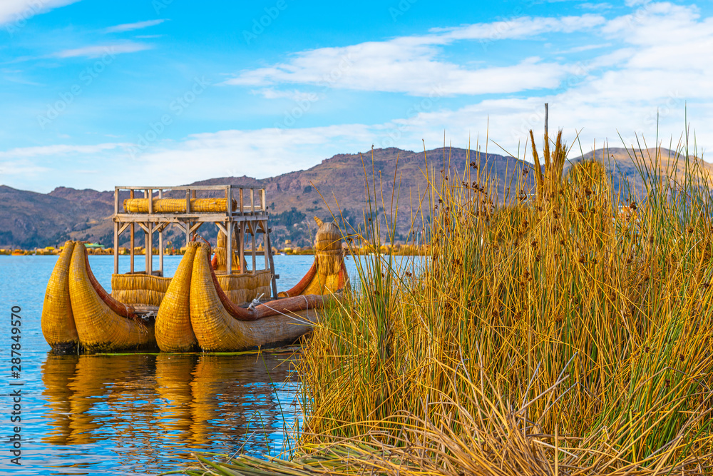 A totora reed boat by the Uros floating islands at sunrise with the Andes mountain range in the background near Puno, Peru, South America.