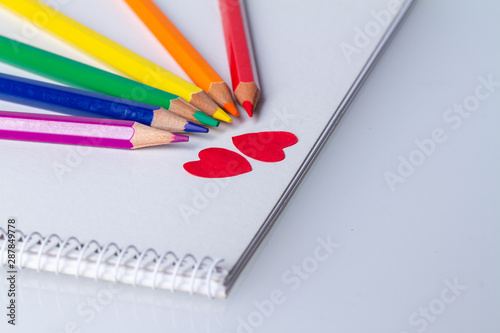 rainbow of coloring pencils around two red paper hearts on a booklet