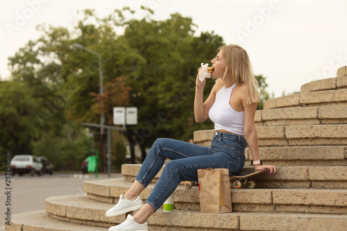 Pretty young blonde funny woman eating hamburger outdoor on the street.