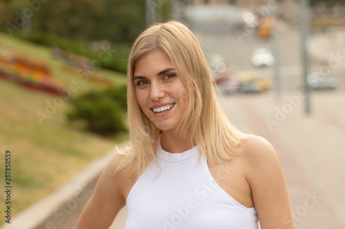 Outdoors lifestyle fashion portrait of happy stunning blonde girl. Beautiful smile. Walking to the city street. Long light hair. Joyful and cheerful woman. Happiness.