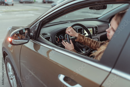 A girl driving a car, looks in a side view mirror, parking at a shopping center, turning at an intersection, turning on a turn signal on a car. Left turn. Woman in a leather jacket.
