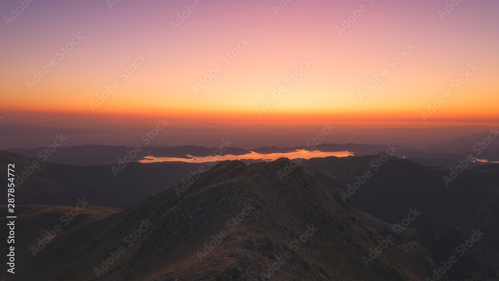 Burning dawn above Plastiras lake where the lake is glowing red from the sky Burning dawn above Plastiras lake where the lake is glowing red from the sky