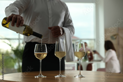 Waiter pouring wine into glass in restaurant, closeup