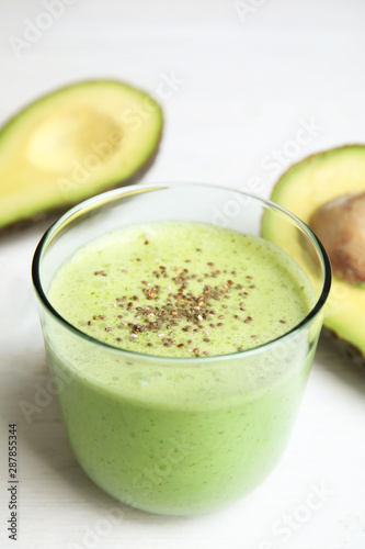 Glass of tasty avocado smoothie with chia seeds on white wooden table