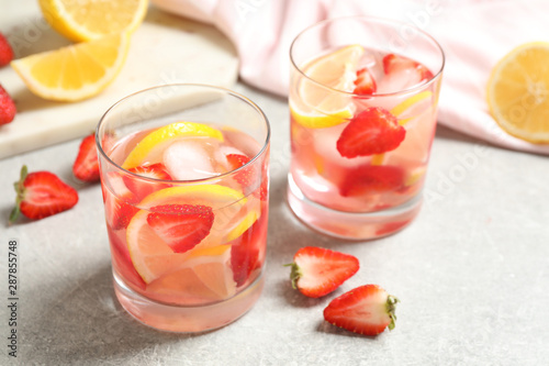 Tasty refreshing drink with strawberries and lemon on light grey table