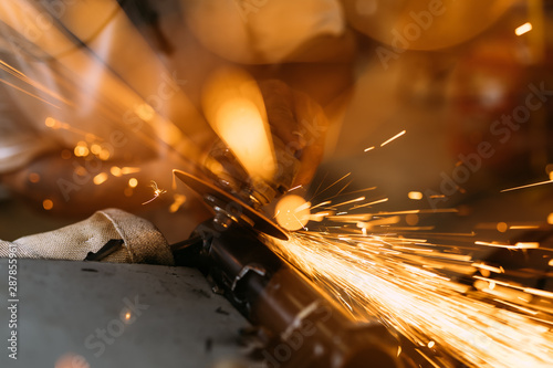 Worker cutting, grinding and polishing motorcycle metal part with sparks indoor workshop, close-up