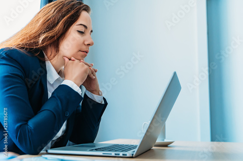 Tired business woman looks at laptop screen propping her head with her hands, recycling at work, stress concept