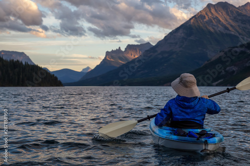 Adventurous Man Kayaking in Glacier Lake surrounded by the beautiful Canadian Rocky Mountains during a cloudy summer sunset. Taken in Upper Waterton Lake  Alberta  Canada.