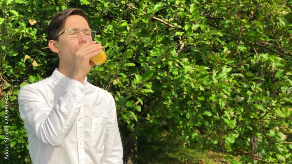 Young handsome man drinks orange juice and smile in the garden enjoying life. Concept. Vegetarianism. Healthy life. Freelance Young handsome man drinks orange juice and smile in the garden enjoying life. Concept. Vegetarianism. Healthy life. Freelance