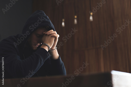 Cuadro en lienzo Man detained in handcuffs at table indoors, space for text