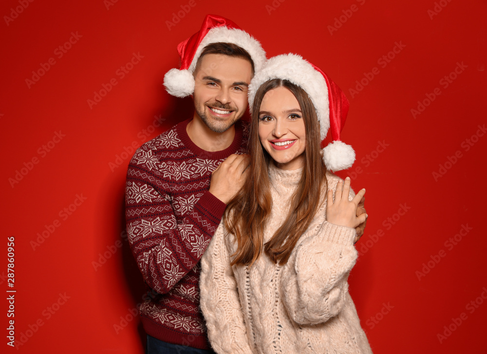 Couple wearing Christmas sweaters and Santa hats on red background Couple wearing Christmas sweaters and Santa hats on red background