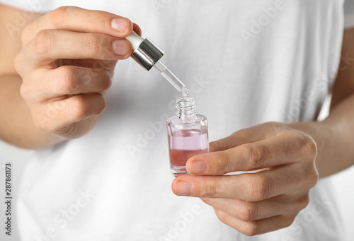 Young woman dripping rose essential oil into glass bottle, closeup