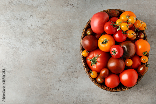 Fresh ripe tomatoes in wicker bowl on grey table, top view. Space for text