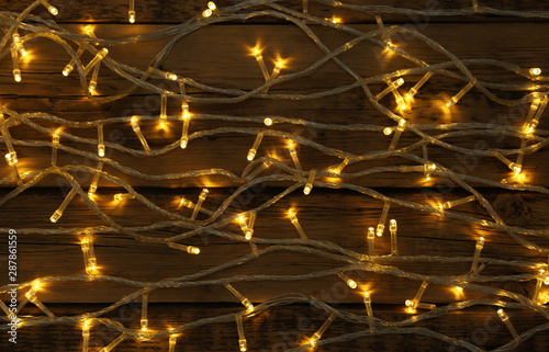 Glowing Christmas lights on wooden background, top view