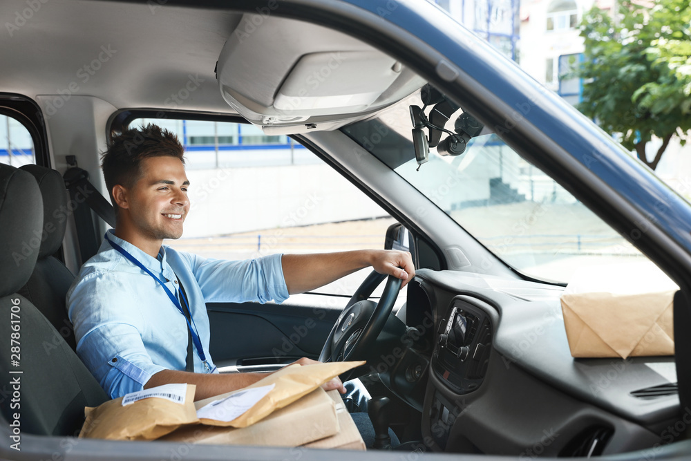 Fototapeta premium Young courier with parcels in delivery car