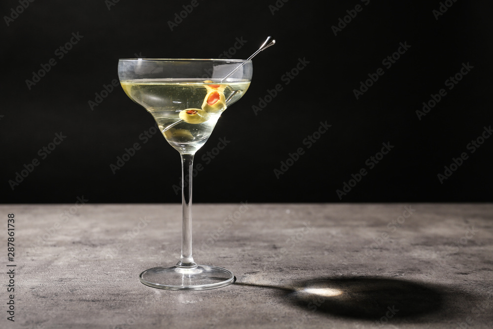 Glass of Classic Dry Martini with olives on grey table against black background. Space for text