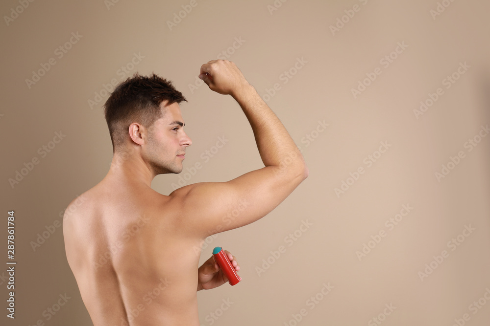 Fototapeta premium Young man applying deodorant to armpit on beige background. Space for text