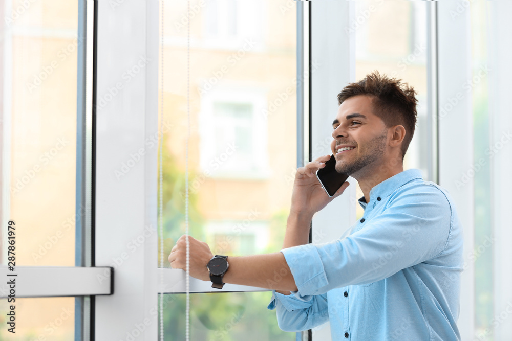 Portrait of handsome young man talking on mobile phone near window Portrait of handsome young man talking on mobile phone near window